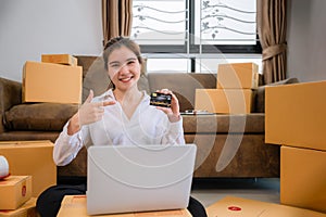 Beautiful Asian woman is online business owner sitting smile and using computer laptop with credit card showing in home office