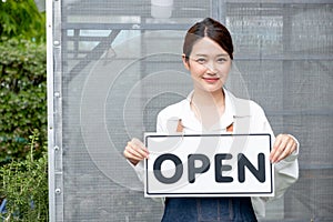 Beautiful Asian woman present banner with word open in front of green house and happy emotion relate with re-open the business photo