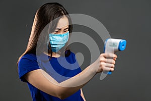 Beautiful asian woman in protective medical mask uses an electronic thermometer to measure temperature. Flu epidemic