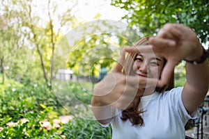 A beautiful asian woman raising hands and playing with camera in park