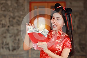Beautiful Asian woman in red Chinese dress traditional cheongsam qipao with gesture of opening red envelope with money, she