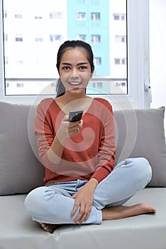 Beautiful asian woman with remote control watching television while sitting
