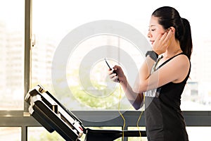 Beautiful asian woman running treadmill use smartphone listening