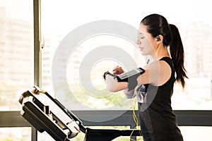 Beautiful asian woman running treadmill use smartwatch listening