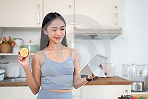 A beautiful Asian woman is searching for healthy recipes online on her tablet in the kitchen