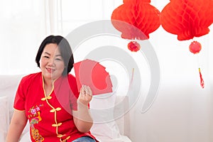 Beautiful Asian woman sit on bed at home show many red envelops with happy  Woman in Red Chinese Costume traditional with Lunar