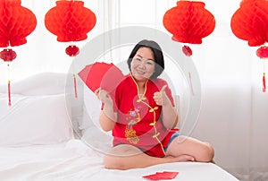 Beautiful Asian woman sit on bed at home show many red envelops with happy  Woman in Red Chinese Costume traditional with Lunar