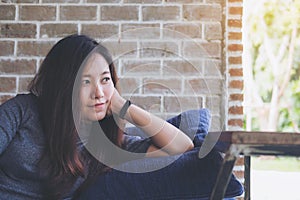 A beautiful Asian woman sit with chin resting on her hands above a blue pillow with feeling happy and relax in cafe