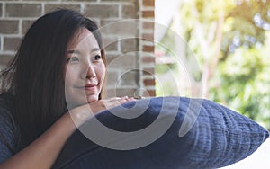 A beautiful Asian woman sit with chin resting on her hands above a blue pillow with feeling happy and relax in cafe