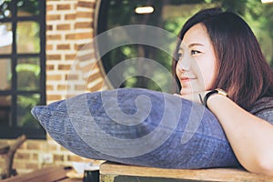 A beautiful Asian woman sit with chin resting on her hands above a blue pillow with feeling happy and relax in cafe