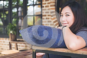 A beautiful Asian woman sit with chin resting on her hands above a blue pillow with feeling happy and relax in cafe