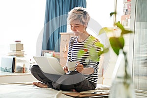 Beautiful Asian woman sitting on bed & working from home on laptop