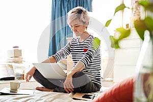 Beautiful Asian woman sitting on bed & working from home on laptop