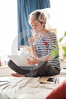 Beautiful Asian woman sitting on bed & working from home on laptop