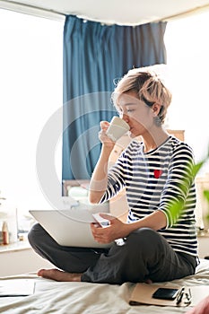 Beautiful Asian woman sitting on bed & working from home on laptop