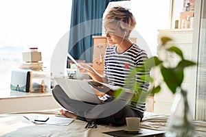 Beautiful Asian woman sitting on bed & working from home on laptop