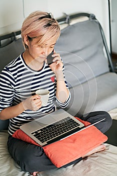 Beautiful Asian woman sitting on bed & working from home on laptop