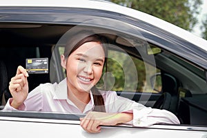 Beautiful Asian woman sitting in a car, happy smile Hold a credit card to pay for car repairs.