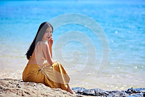 Beautiful asian woman sitting on the stones near the sea
