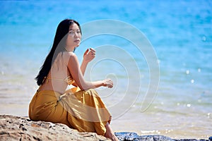 Beautiful asian woman sitting on the stones near the sea