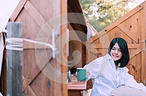 Beautiful asian woman sitting at tent and drinking coffee in the morning,Enjoys of resting time,Happy and smiling