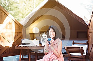 Beautiful asian woman sitting at tent and drinking coffee in the morning,Enjoys of resting time,Happy and smiling