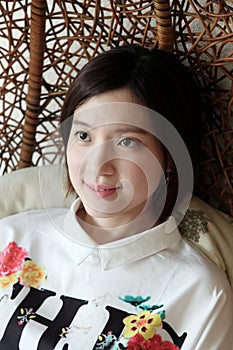 Beautiful Asian woman sitting in a wicker chair looking sideways