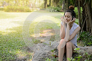 Beautiful asian woman smile and relaxing by listen to music from stereo headphones in public park. with copy space