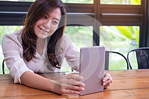 A beautiful Asian woman with smiley face holding and using tablet pc in modern cafe