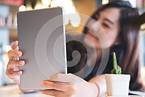 A beautiful Asian woman with smiley face holding and using tablet pc in modern cafe