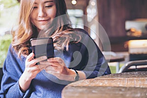 A beautiful Asian woman with smiley face using and looking at a black smart phone