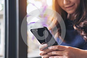 A beautiful Asian woman with smiley face using and looking at a black smart phone