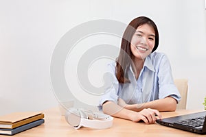 Beautiful asian woman smiling at desk office with laptop, headphones, notepad, hot coffee mug on the table