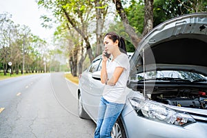 Beautiful asian woman stands beside a broken car. She talking on cell phone for assistance