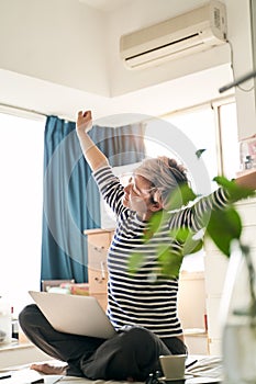 Beautiful Asian woman stretching arms on bed during working from home on laptop