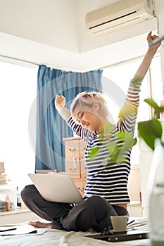 Beautiful Asian woman stretching arms on bed during working from home on laptop