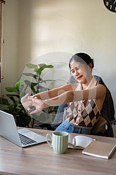 A beautiful Asian woman is stretching her arms to relax after finishing her work at her desk