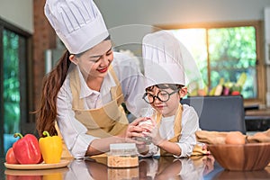 Beautiful Asian woman teaching cute little boy with eyeglasses to drink milk in kitchen at home together. Lifestyles and Family.