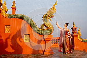 Beautiful Asian woman with Thai traditional dress stand with action of Thai dance in front of the naga sculpture in temple area