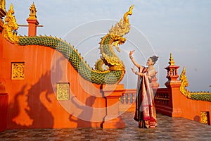 Beautiful Asian woman with Thai traditional dress stand with action of Thai dance in front of the naga sculpture in temple area