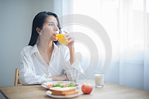 Beautiful asian woman took a sip of juice from the glass in her hand and turned her gaze towards the copy space on the table