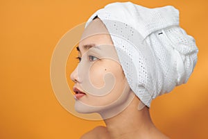 Beautiful Asian woman with a towel on her head over orange background. Spa Beauty concept