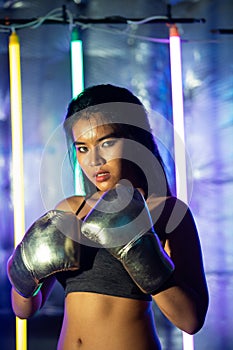 Beautiful Asian Woman is training and punching with Silver gold Mitts Gloves. Office Girl exercises in Modern color Neon Muay Thai