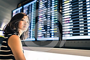 Beautiful Asian woman traveler at flight information screen in an airport, travel or time concept