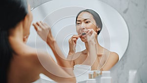 Beautiful Asian Woman Uses Dental Floss to Clean Her Natural White Teeth, Smiles in Bathroom Mirro