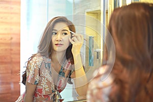 Beautiful Asian woman using eyebrow pencil make up in front mirror