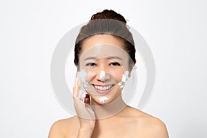 Beautiful Asian woman is using a facial foam to wash cosmetics off her face on a white background