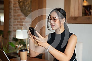 A beautiful Asian woman is using her phone, responding to messages while sitting in a coffee shop