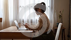 A beautiful Asian woman using her smartphone, responding to messages while working remotely at cafe