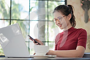 Beautiful asian woman using smart phone and laptop computer for online shopping, happy and relax at workplace coffee shop.